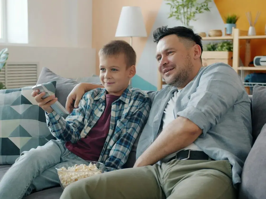 Father and son relaxing on the sofa watching IPTV together with popcorn